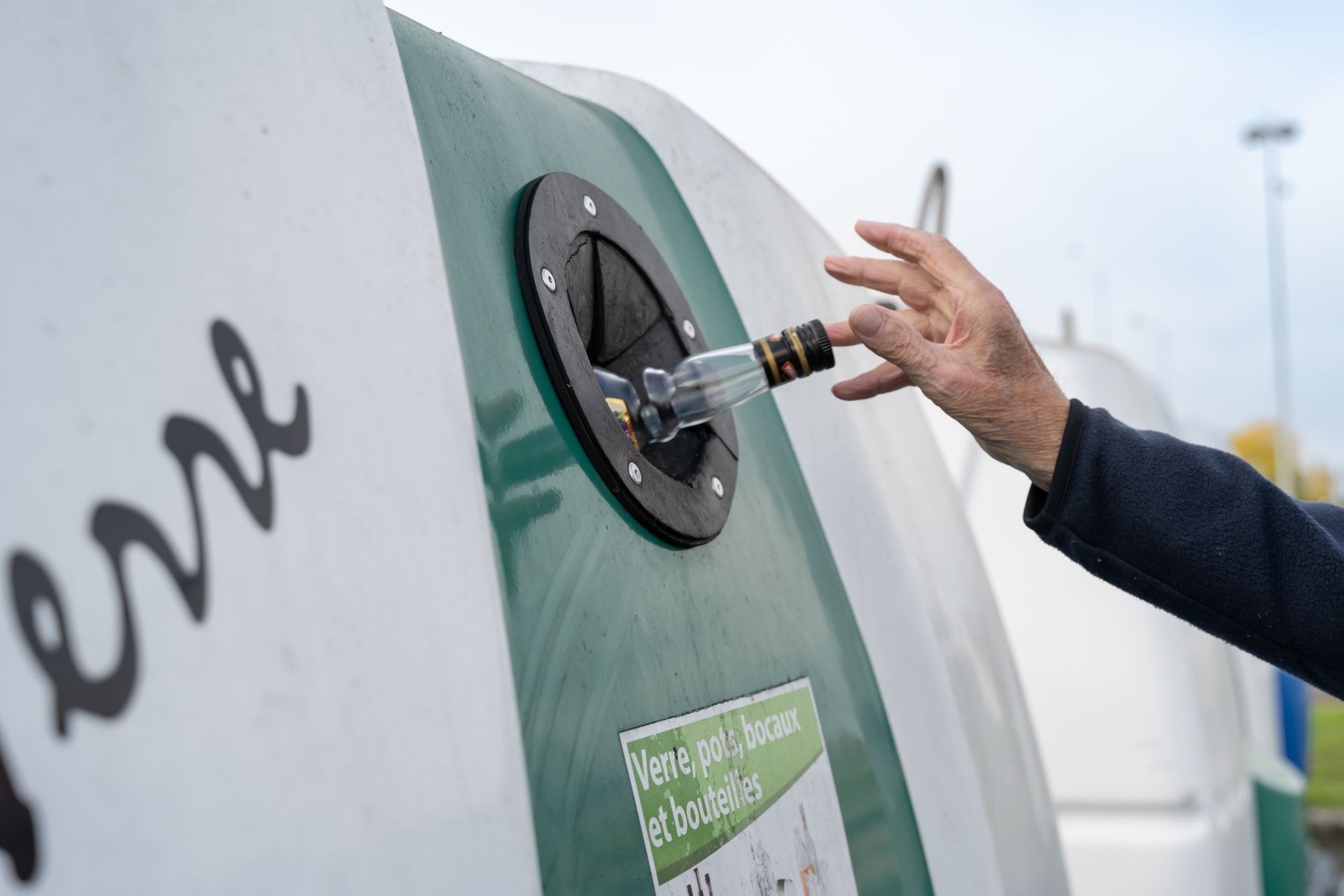 Une main déposant une bouteille en verre dans un conteneur de recyclage.