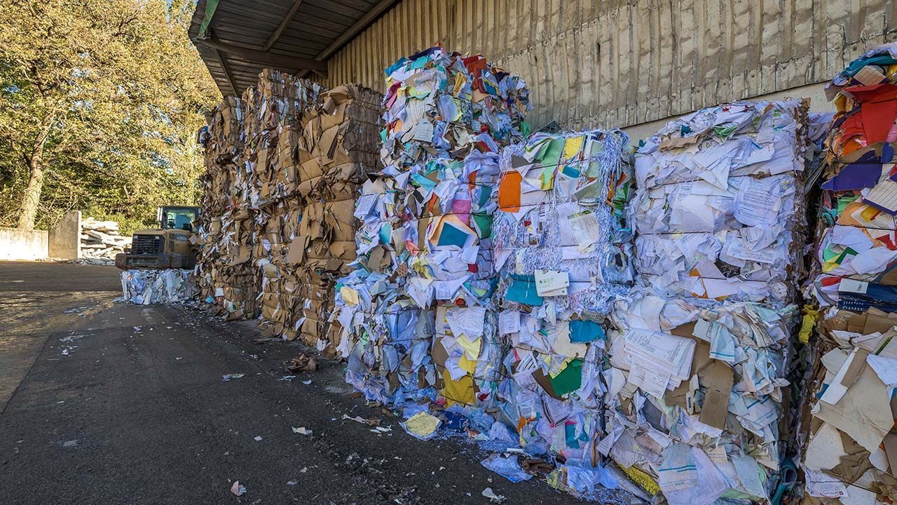 Piles de cartons et papiers compactés devant un hangar de tri.