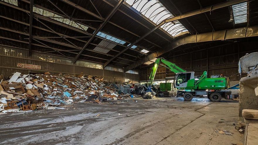 Vue en grand-angle du hangar de traitement des déchets par une grue à pinces.