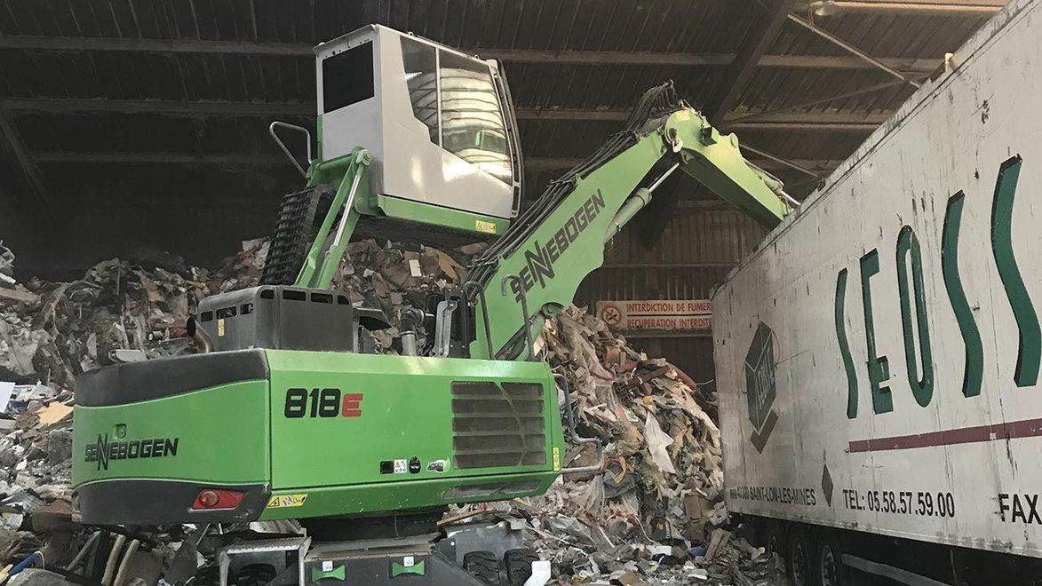 Une grue à pince vidant un camion-benne rempli de déchets.