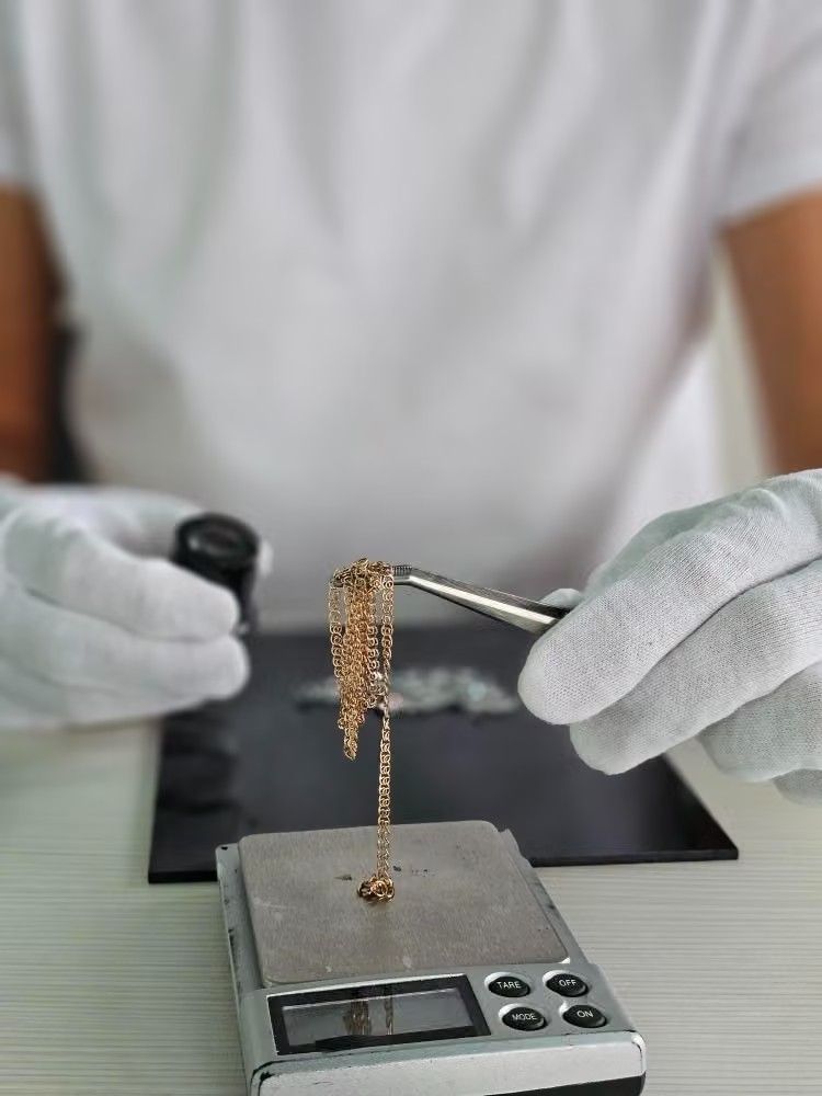 Manos enguantadas sosteniendo una pequeña muestra sobre una balanza digital en un entorno de laboratorio.