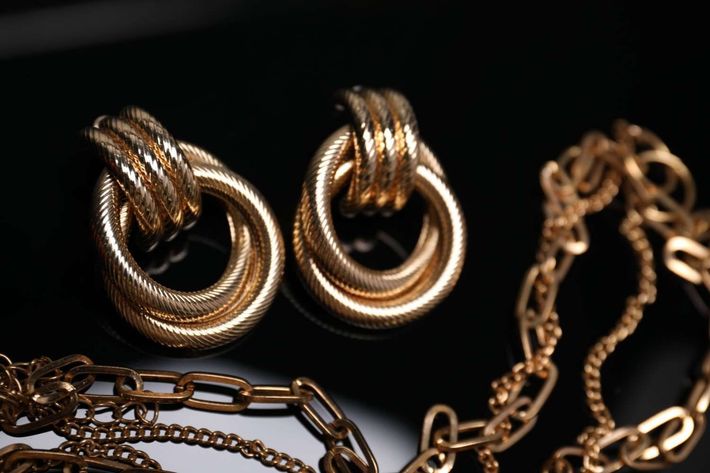 Pendientes de aro dorados y collar de cadena sobre fondo negro.