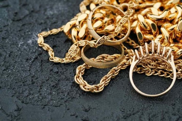 Anillos de oro y collares de cadena sobre una superficie oscura texturizada, con un anillo de púas a la derecha.