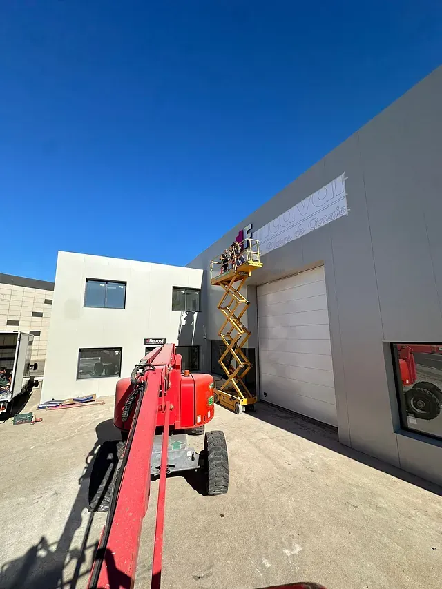 Un elevador de tijera rojo está estacionado frente a un edificio.
