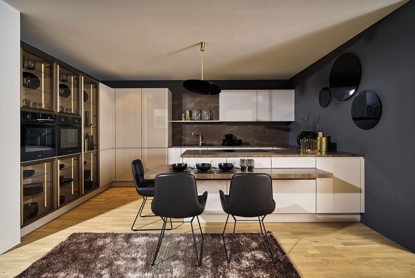 Présentation de la cuisine blanche laquée en angle sur murs aux tons foncés avec chaises hautes noires autour d'une table intégrée au plan de travail.