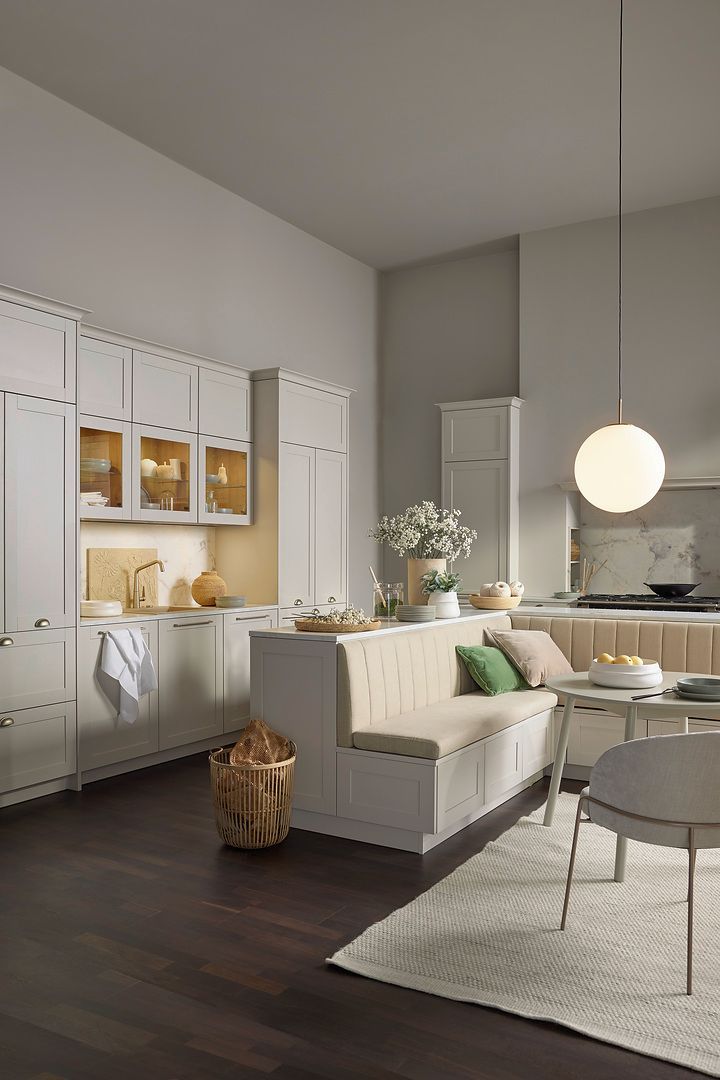 Présentation de la cuisine couleur blanc. Coin repas en angle avec assise intégré derrière un meuble de la cuisine.