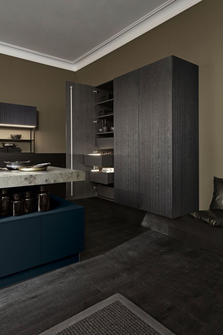 Présentation d'un meuble de rangement tout en hauteur avec un battant ouvert et d'une partie de l'îlot central en effet marbre.