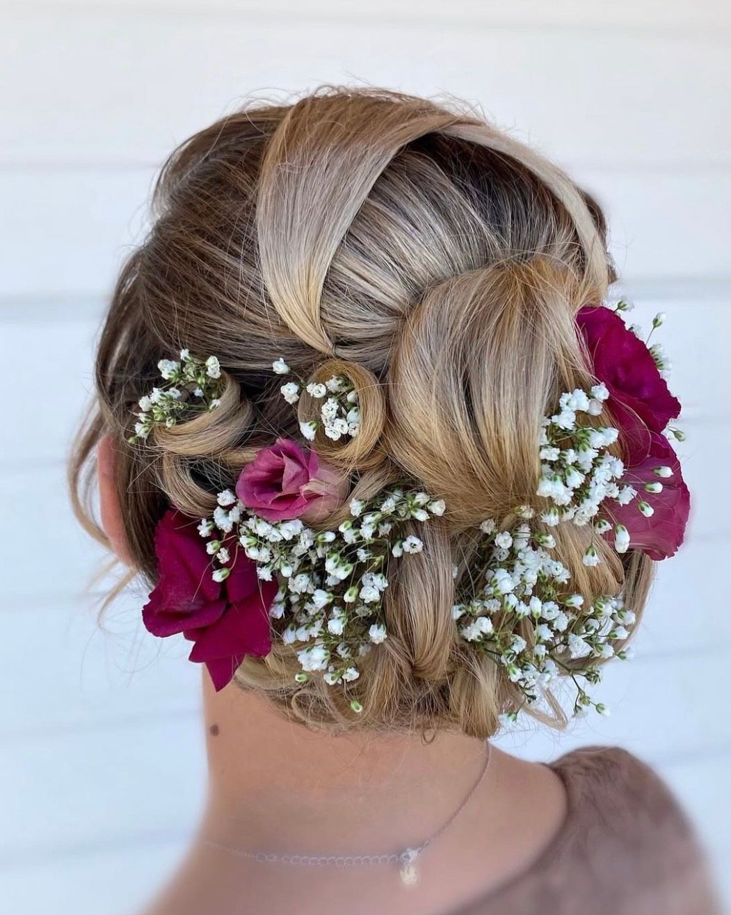 Une femme avec des fleurs dans les cheveux se tient devant un mur blanc.