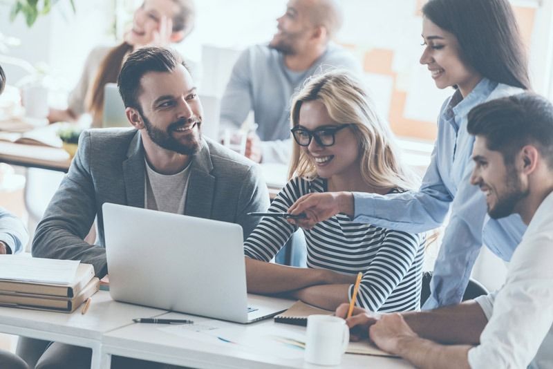 Un grupo de personas están sentadas alrededor de una mesa mirando una computadora portátil.