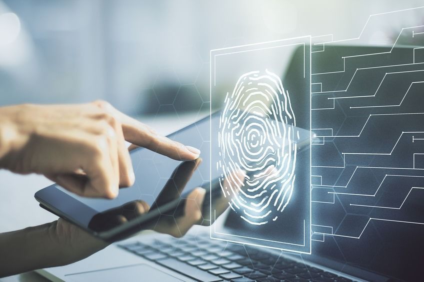 Una persona sostiene un teléfono celular frente a una computadora portátil.
