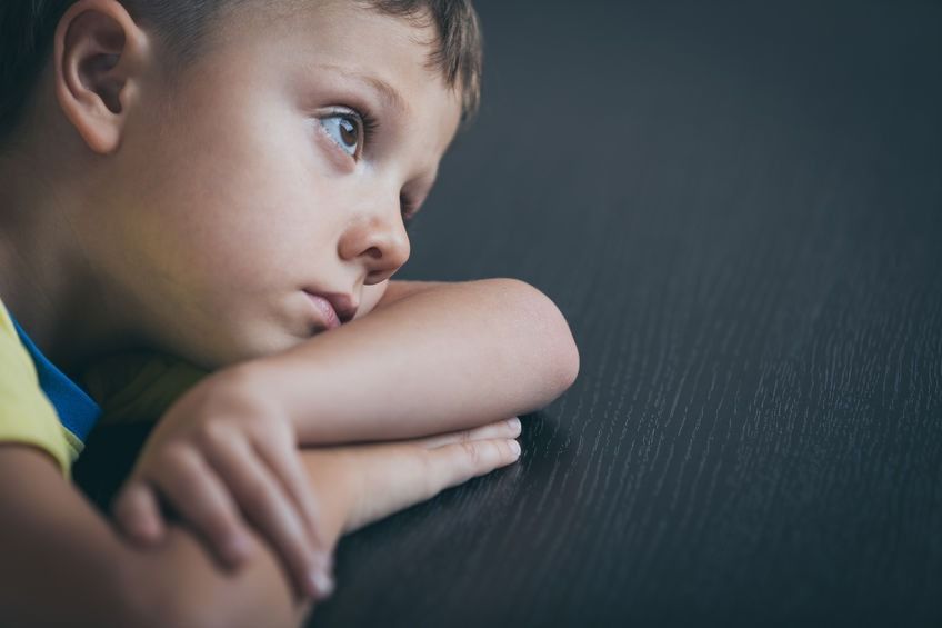 Un niño pequeño está sentado en una mesa con la cabeza apoyada en su brazo.