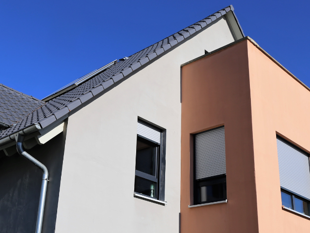 Bâtiment moderne de deux étages avec un toit gris et des murs extérieurs de couleur beige/pêche sous un ciel bleu vif.