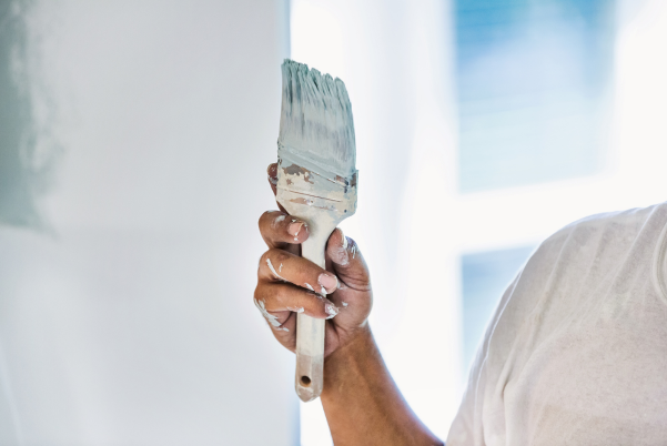 Main tenant un pinceau appliquant de la peinture bleue sur un mur blanc.