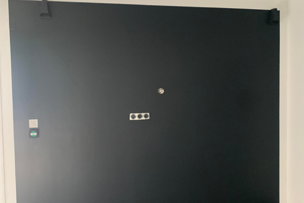 Porte d'appartement noire avec judas, clavier et boutons de contrôle d'entrée, encadrée par des murs blancs.