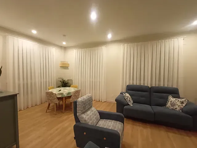 Una sala de estar con sofá, silla, mesa y cortinas.