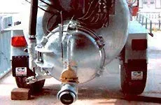 Remolque verde lleno de follaje verde detrás de un tractor naranja sobre una superficie beige.