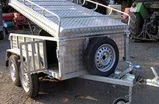 Varios remolques utilitarios plateados estacionados cerca de un edificio moderno en un día soleado.