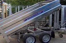 Remolque agrícola de color naranja sobre césped verde, con como telón de fondo una ladera rocosa y follaje.