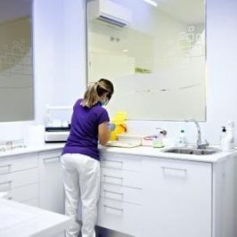 Una mujer con una camisa morada y pantalones blancos está limpiando un mostrador en una cocina.