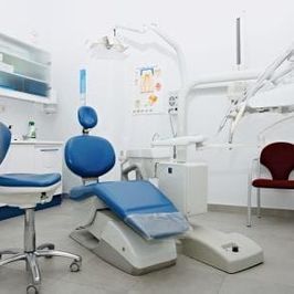 Un consultorio dental con una silla dental azul y una silla roja.
