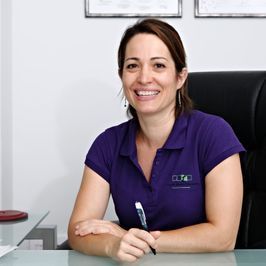 Una mujer con una camisa morada sonríe mientras está sentada en un escritorio.