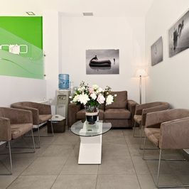 Una sala de espera con un sofá, sillas, una mesa de café y un jarrón de flores.