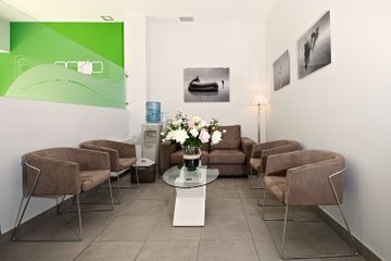 Una sala de espera con un sofá, sillas, una mesa de café y un jarrón de flores.