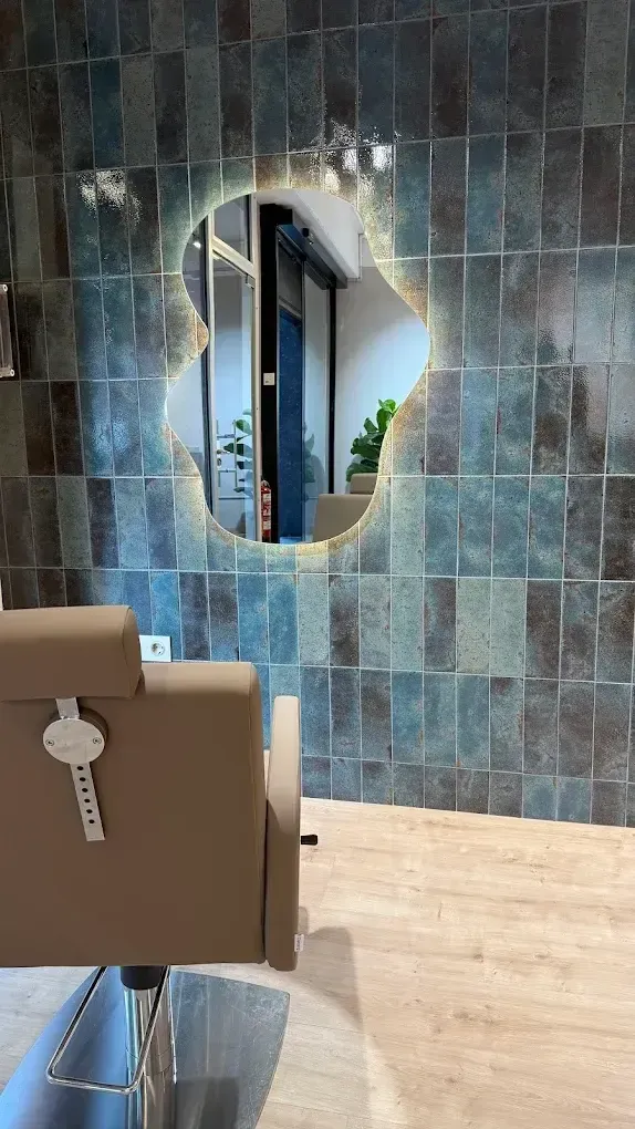 Silla de salón moderna frente a una pared de azulejos azules con un espejo ovalado y suelo de madera clara.