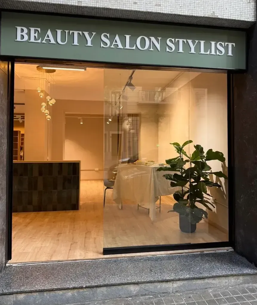Fachada de salón de belleza con cristal, iluminación cálida y una planta en maceta.