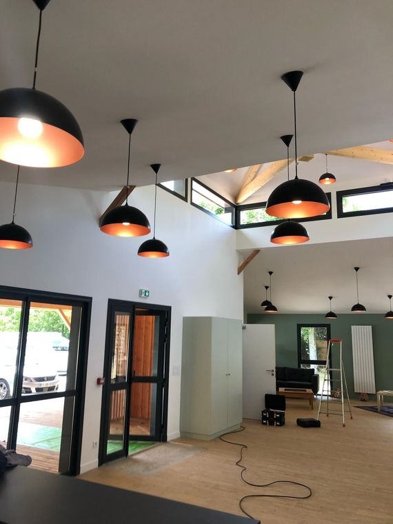 Vue intérieure d'une pièce avec plusieurs suspensions lumineuses noires et cuivrées, un parquet et des murs blancs.