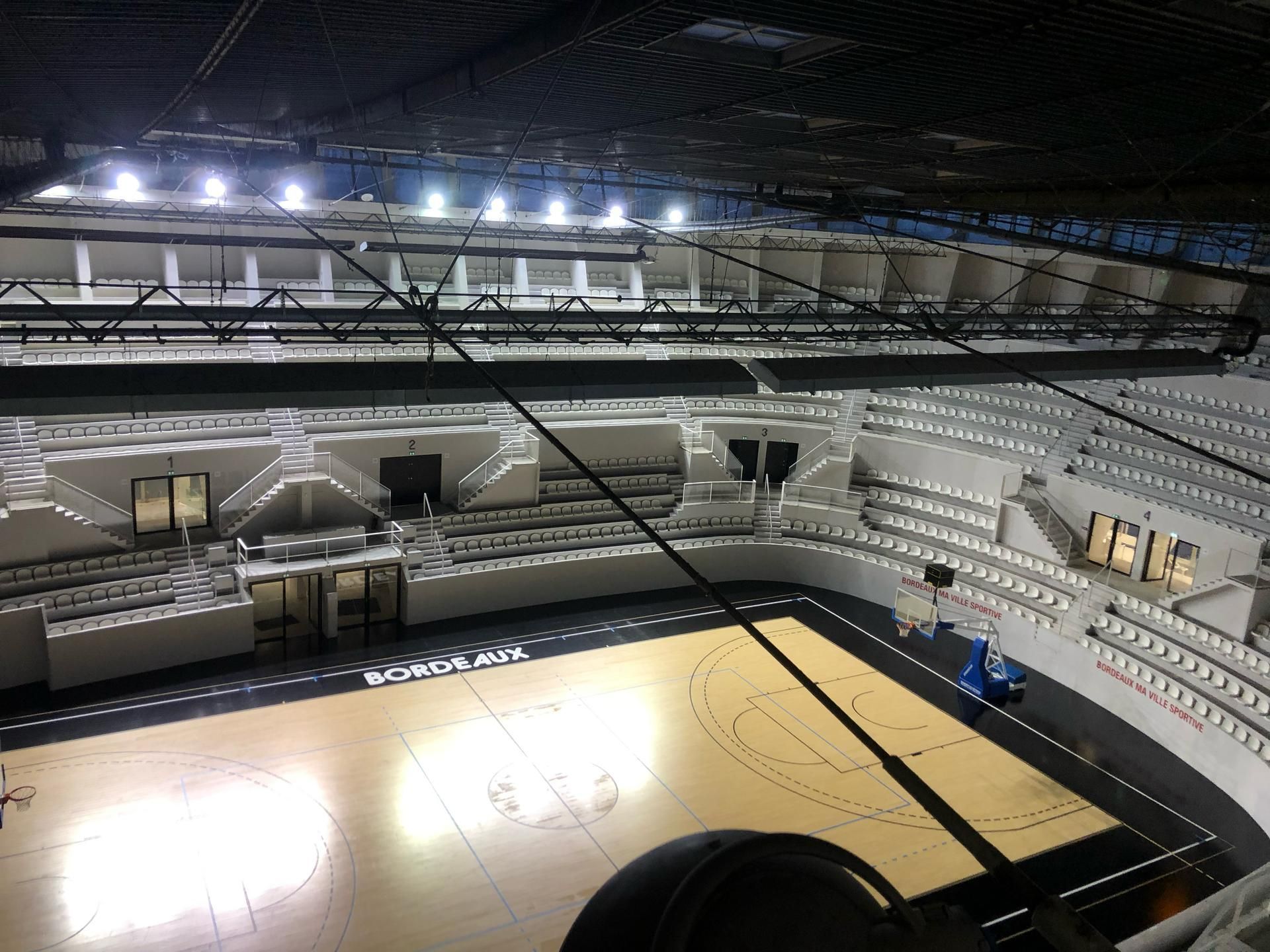 Arène de basketball, terrain vide, gradins, éclairage zénithal.