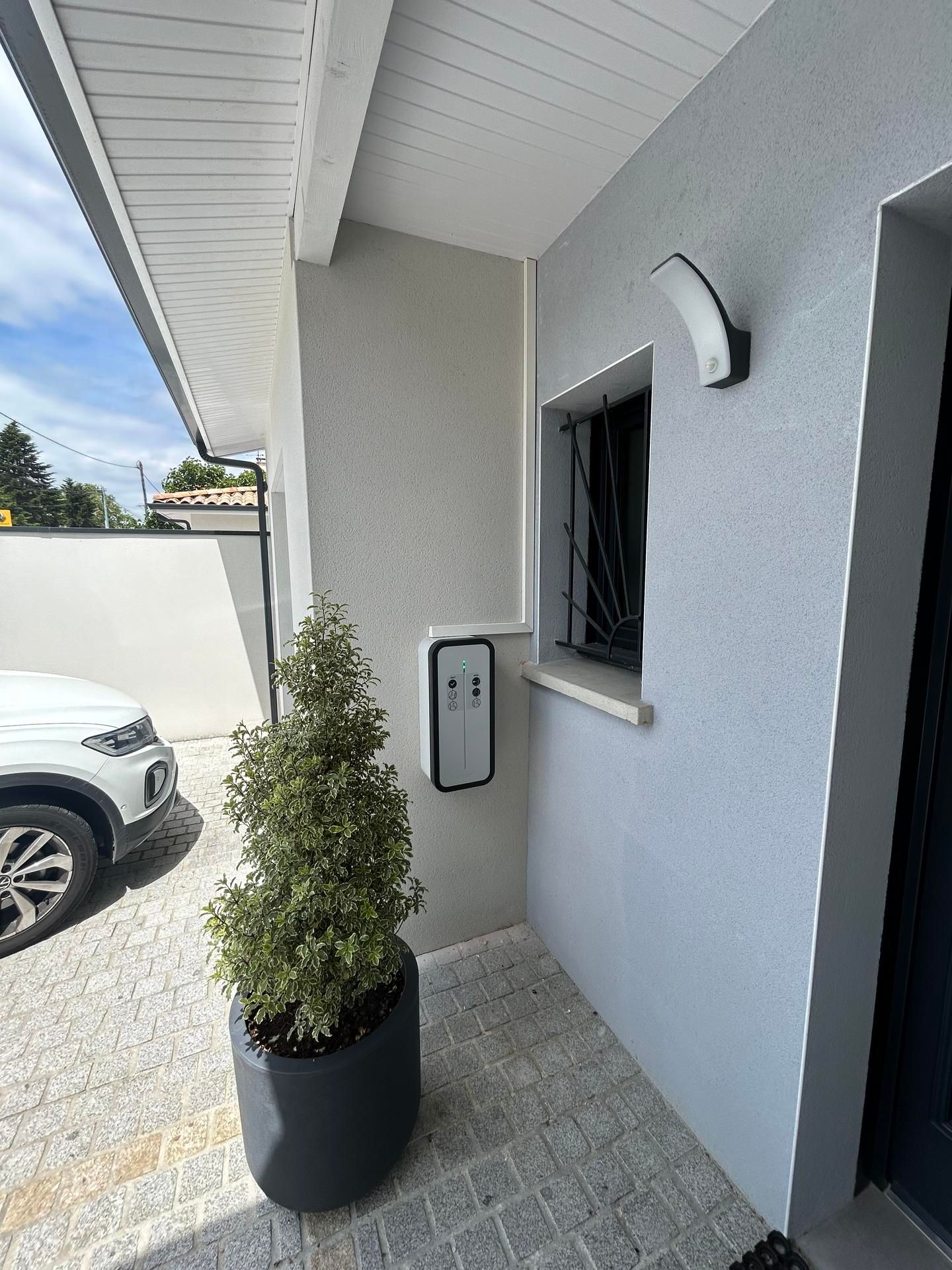 Extérieur d'une maison avec une borne de recharge pour véhicule électrique fixée au mur.