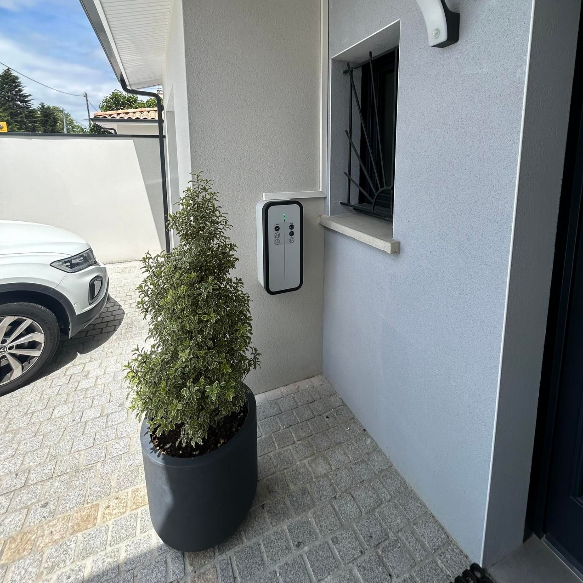 Extérieur d'une maison avec une borne de recharge pour véhicule électrique fixée au mur.