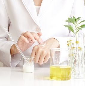 Una mujer con una bata de laboratorio está usando una pipeta para verter líquido en un vaso.