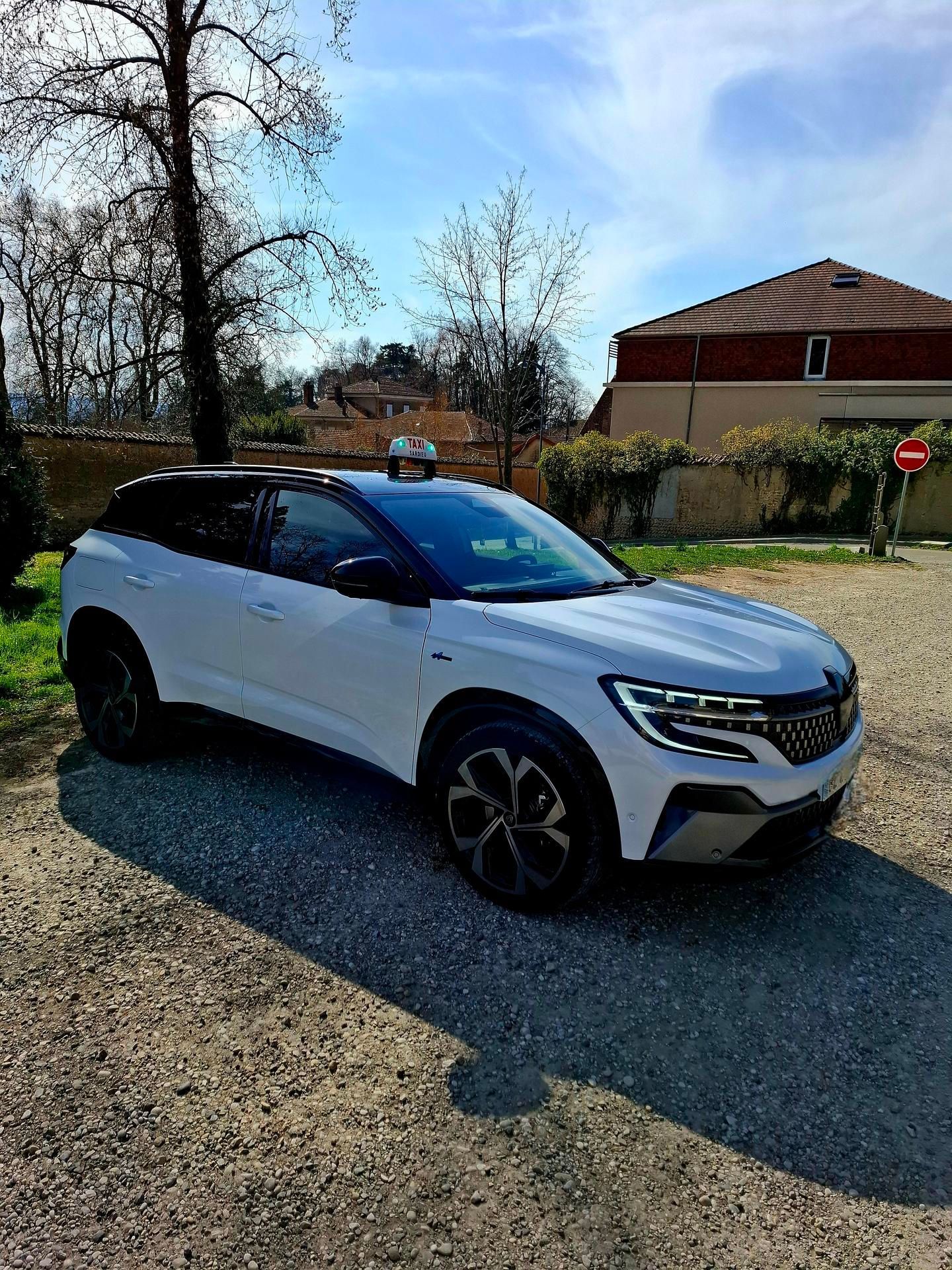 SUV blanc garé sur une allée de gravier à côté d'une maison par une journée ensoleillée.