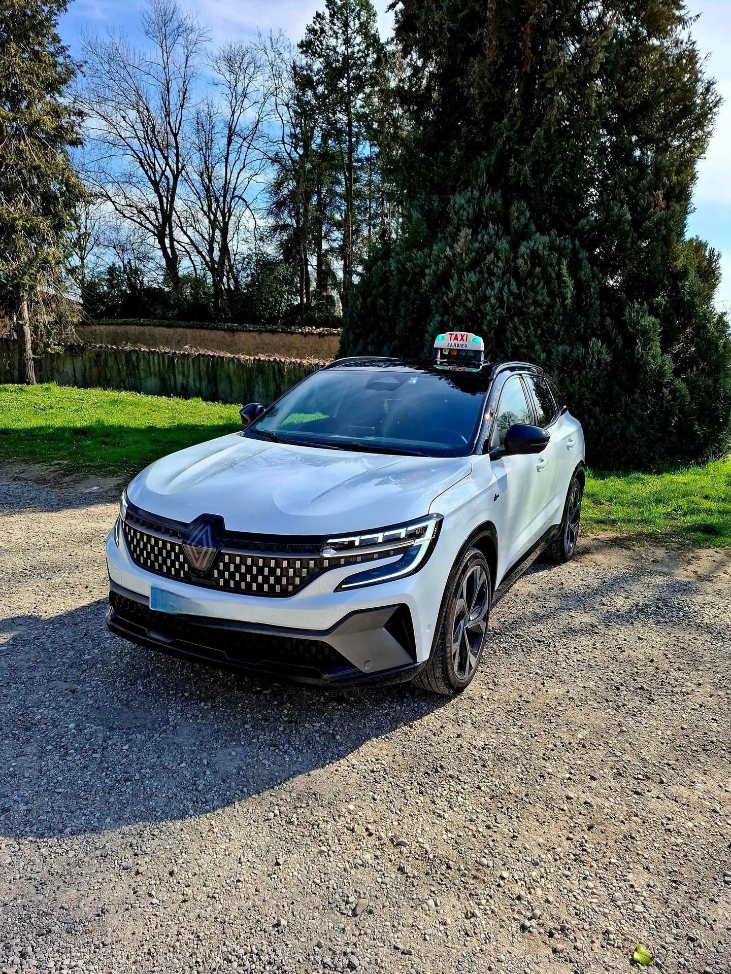 Un SUV Renault blanc garé sur du gravier, à côté d'arbres et d'herbe.
