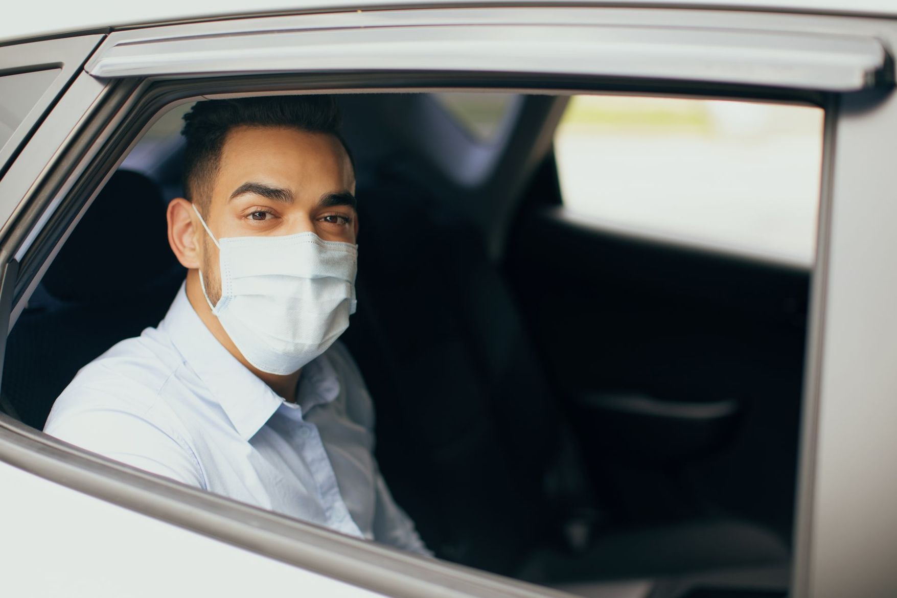 Passager masqué assis dans une voiture, regardant par la fenêtre.