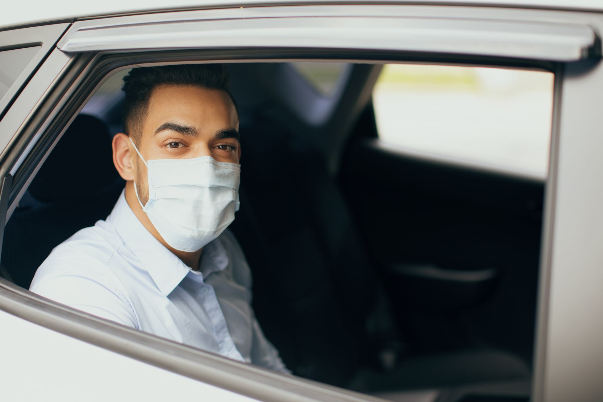 Une personne masquée, assise dans une voiture, regarde par la fenêtre.