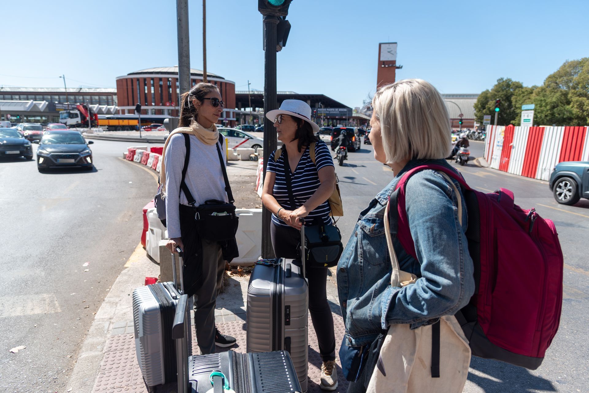 Trois voyageurs avec des valises à roulettes traversent une rue près d'un terminal de ferry.