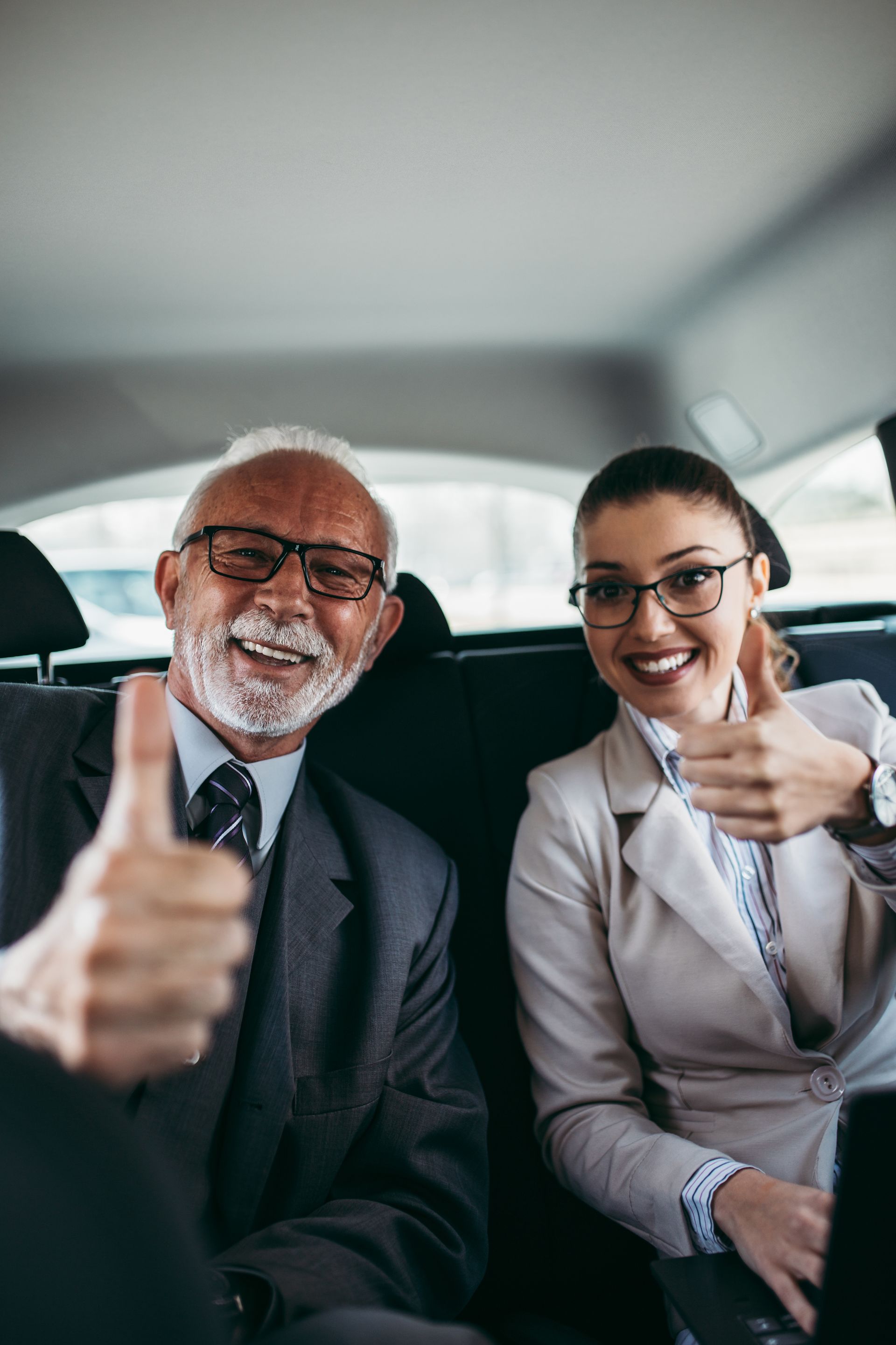 Deux collègues de travail sourient et lèvent le pouce à l'intérieur d'une voiture.