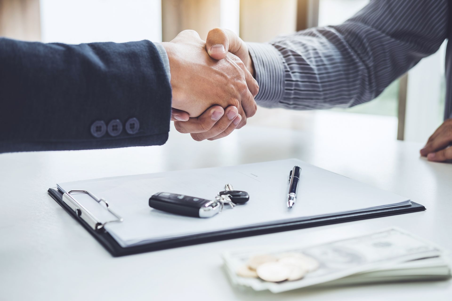 Deux personnes se serrent la main au-dessus d'un bureau où se trouvent un bloc-notes, des clés et un stylo, suggérant un accord commercial.