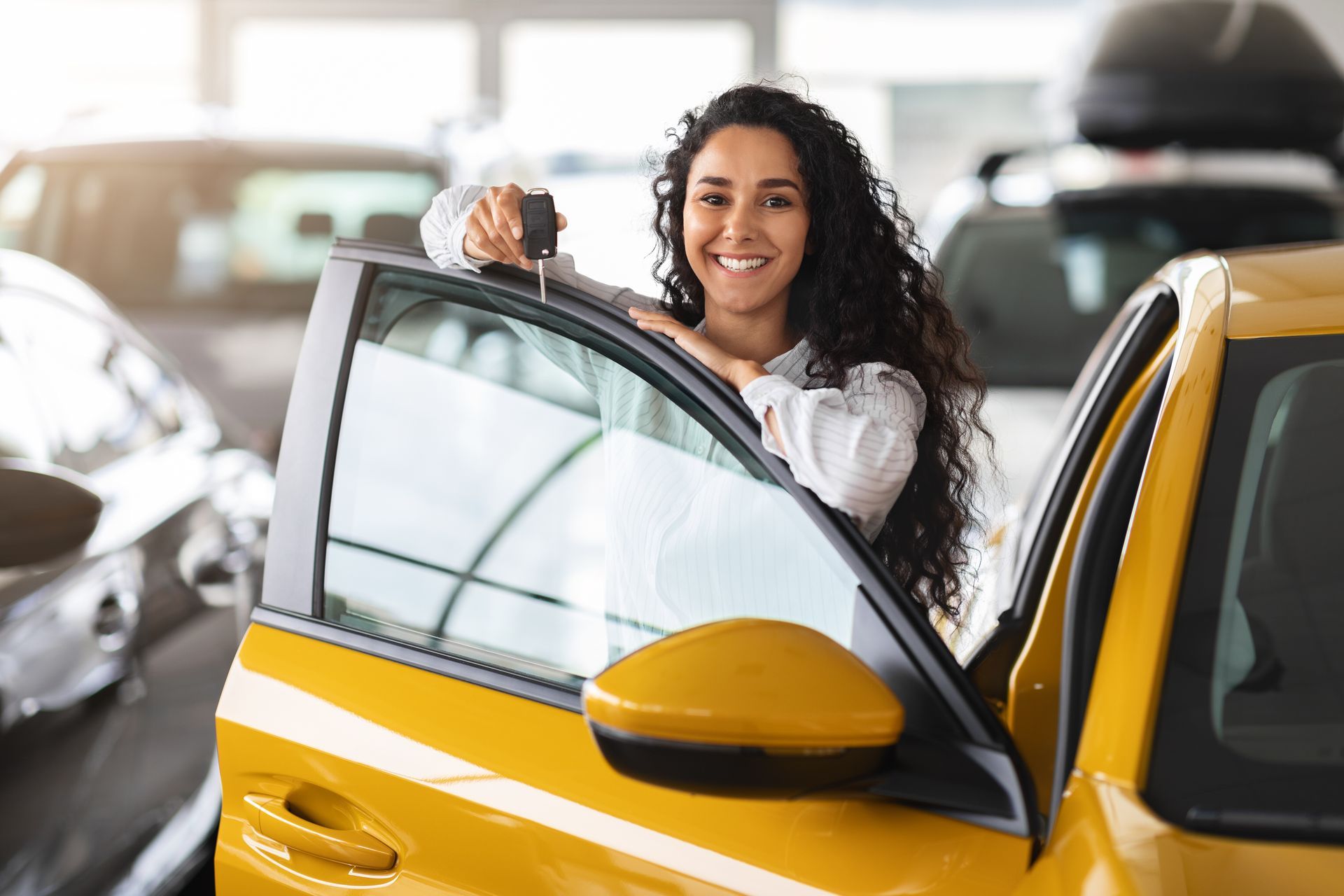 Une femme sourit à côté d'une voiture jaune dans une salle d'exposition