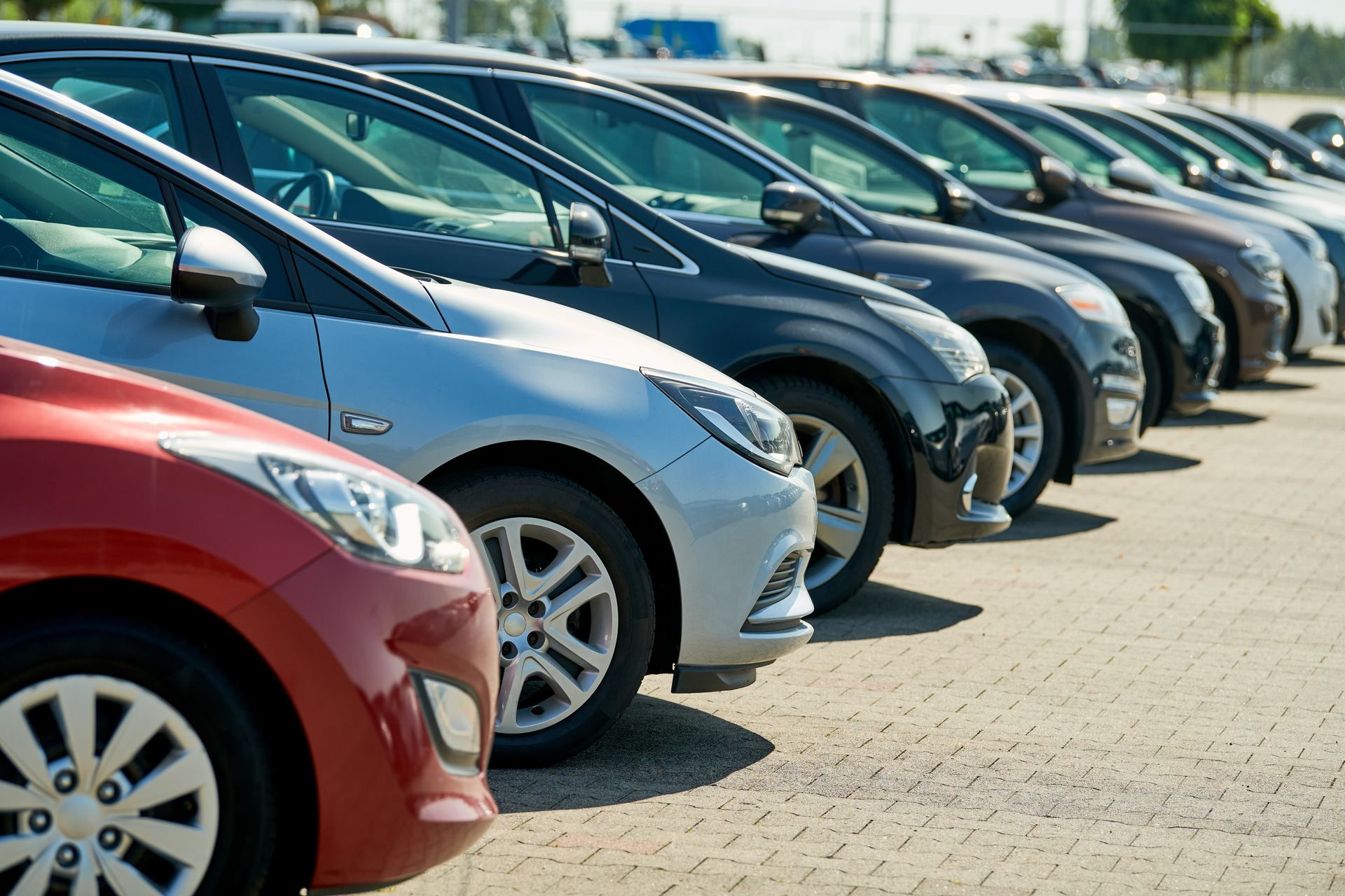 Rangée de voitures garées sur le parking d'une concession automobile, avec des véhicules rouges, argentés et noirs garés en épi.
