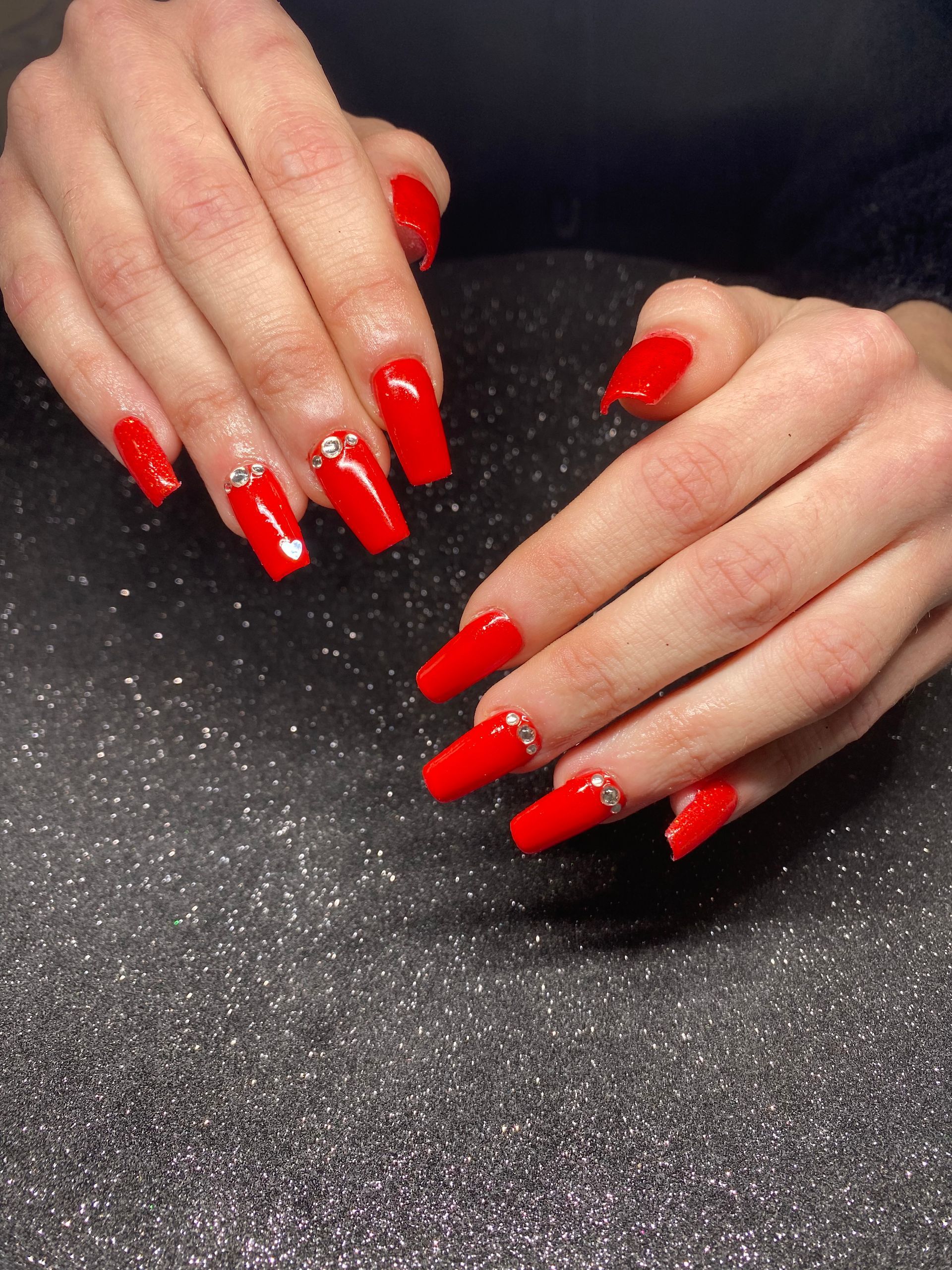 Les mains féminines avec le vernis rouge et les strass.