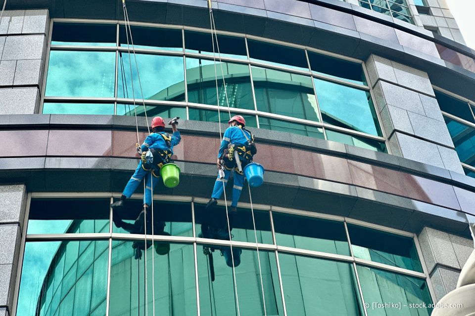 Zwei Fensterputzer an Seilen reinigen ein Glasgebäude.