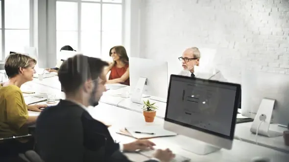 Un grupo de personas están sentadas en escritorios frente a monitores de computadora en una oficina.