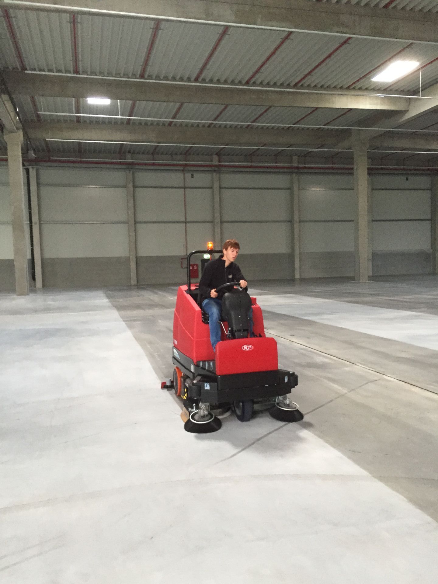 Ein Mann fährt auf einer roten Maschine durch eine große leere Lagerhalle.