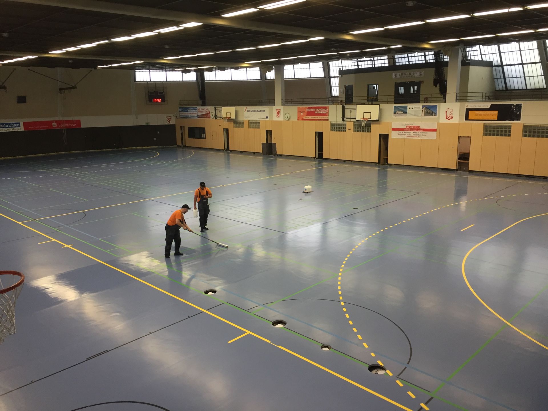 Zwei Männer reinigen den Boden einer Sporthalle.