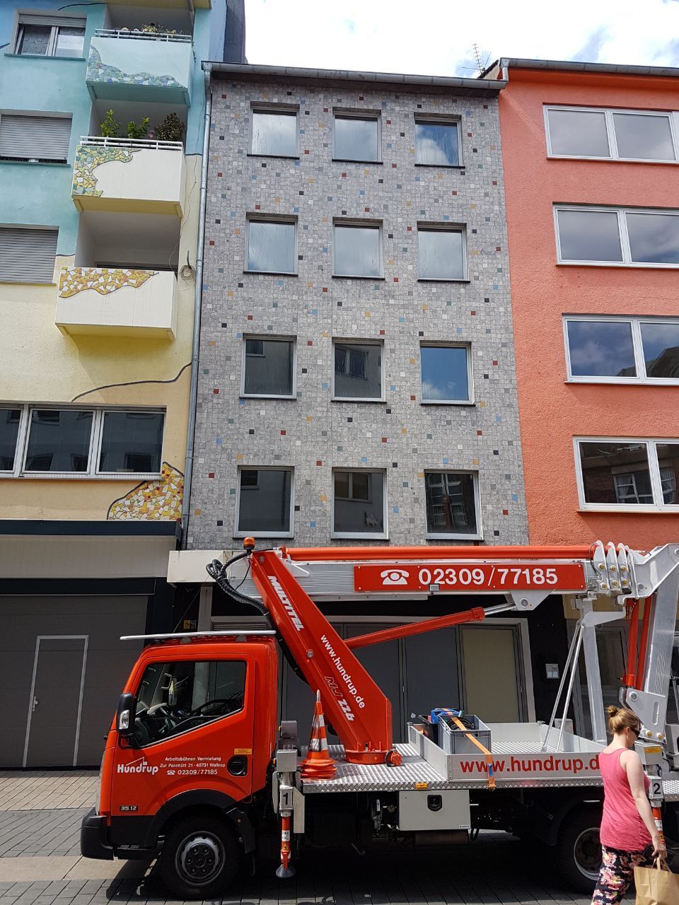 Ein roter LKW mit einer Hebebühne  steht vor einem Gebäude.