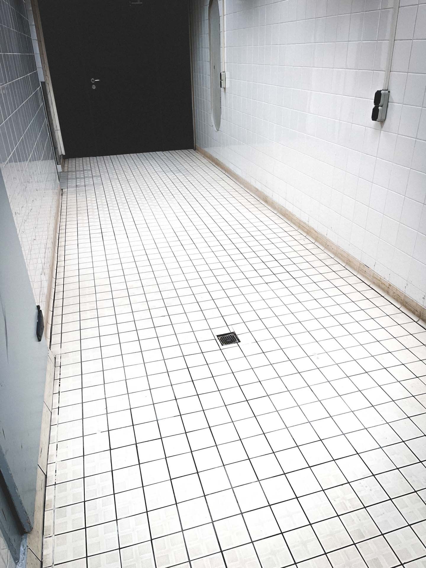 Ein langer Flur mit weißen Fliesen und einer schwarzen Tür.